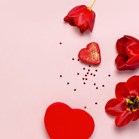 Red tulips, red heart shaped gift box, confetti on pastel pink background top view Flat lay copy space. Mother's Day, Valentines Day, birthday, holiday background. Spring flowers, Lovely greeting card.の写真素材