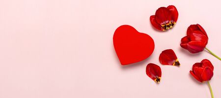 Red tulips, red heart shaped gift box, confetti on pastel pink background top view Flat lay copy space. Mother's Day, Valentines Day, birthday, holiday background. Spring flowers, Lovely greeting card.の写真素材