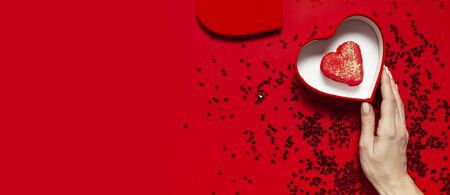 Woman hands holding red gift box shape of heart Heart Shaped Macaroon Cake confetti on red background top view Flat lay. Creative composition for Valentine's Day love concept birthday mother day.の写真素材