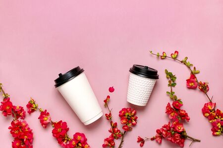 Coffee or tea paper cup, spring branches of red flowers on pink background top view flat lay copy space. Take away coffee cup, mockup. Spring coffee concept, layout for design. Spring flowering.の写真素材