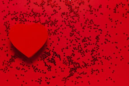 Red gift box in the shape of heart and confetti on red background top view Flat lay. Creative composition for Valentine's Day, love concept, birthday present, mother day, holiday background.の写真素材