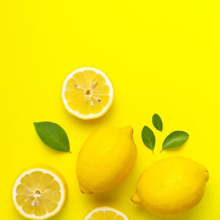 Creative background with fresh lemons and green leaves on bright yellow background. Top view flat lay copy space. Lemon fruit citrus minimal concept vitamin C. Composition with whole, slices of lemons.の写真素材
