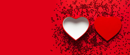 Red gift box in the shape of heart and confetti on red background top view Flat lay. Creative...