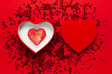 Red gift box in the shape of heart and confetti on red background top view Flat lay. Creative...