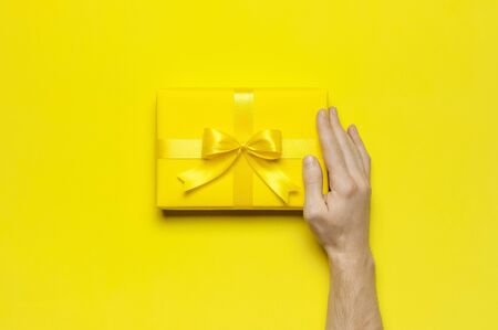 Male hands holding bright yellow gift present box with ribbon on yellow background top view. Flat lay holiday background. Birthday present, March 8, Mother's Day, Valentine's Day. Congratulation.の写真素材