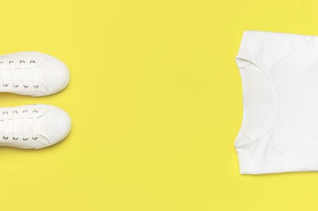 White female fashion sneakers, white T-shirt on yellow orange background. Flat lay top view copy space. Women's shoes. Stylish white sneakers. Fashion blog or magazine concept. Shoe background, sport.の写真素材