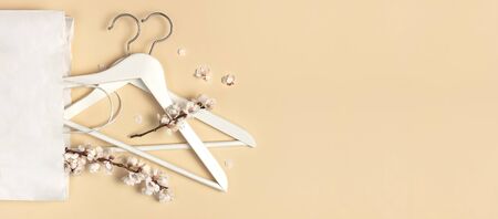 Creative spring sale concept. White wooden hangers with spring flowers white paper bag on beige background top view flat lay. Fashion spring discounts shopping sale store promo design minimalism style.の写真素材
