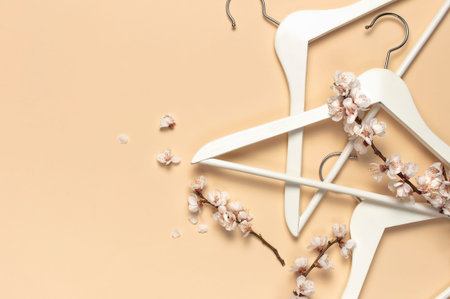 Creative spring sale concept. White wooden hangers with spring sprigs of apricot flowers on beige...