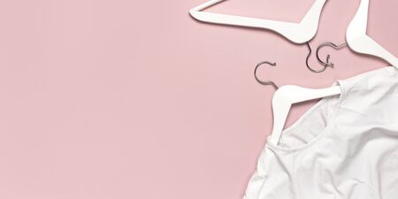 White blank women's t-shirt and white wooden hangers on pink background flat lay top view. T-Shirt Mock-up. Women's T-shirt, clothes, fashion, sale, discounts, store advertising.の写真素材
