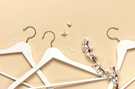 Creative spring sale concept. White wooden hangers with spring sprigs of apricot flowers on beige background top view flat lay. Fashion spring discounts shopping sale store promo design minimalism.の写真素材