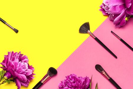 Professional Different makeup brushes with pink spring peonies flowers on yellow pink background flat lay top view copy space. Beauty product, makeup, women's accessory, fashion. Cosmetic makeup Set.の写真素材