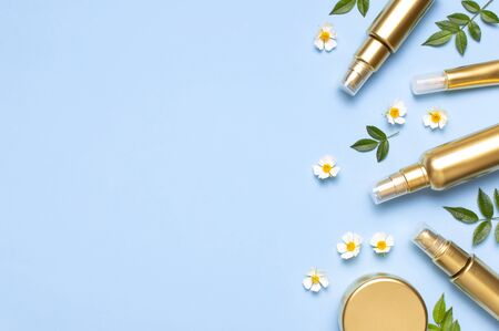 Cosmetic mock up gold bottles. Cosmetics, spring white flowers green leaves on blue background. Cosmetics springtime summer Concept. Flat lay top view copy space. Branding products, beauty background.の写真素材