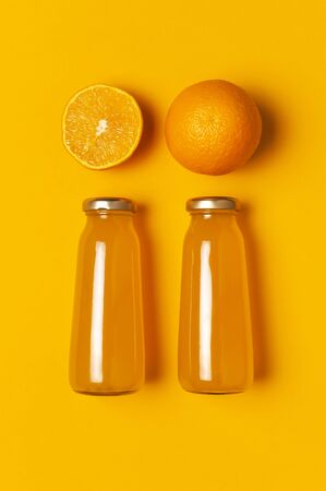 Creative summer concept. Glass bottles with orange juice, fresh sweet orange on yellow background. Healthy food, healthy drink, vitamin C. Flat lay top view. Minimalistic layout with orange juice.の写真素材