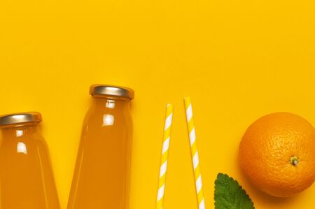 Creative summer concept. Glass bottles with orange juice, fresh sweet oranges, mint leaves and drinking tubs on yellow background. Healthy food, healthy drink, vitamin C. Flat lay top view copy space.の写真素材