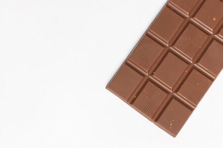Bar of milk chocolate with nuts inside on white background flat lay top view copy space. Minimalistic Chocolate Background. Chocolate, cocoa, sweet treat, sugar, overweight, chocolate addiction.の写真素材