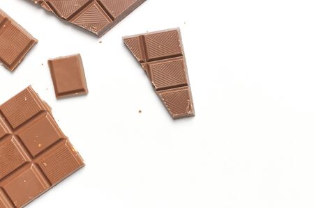Bar and pieces of milk chocolate with nuts inside on white background flat lay top view copy space. Minimalistic Chocolate Background. Chocolate cocoa sweet treat sugar overweight chocolate addiction.の写真素材