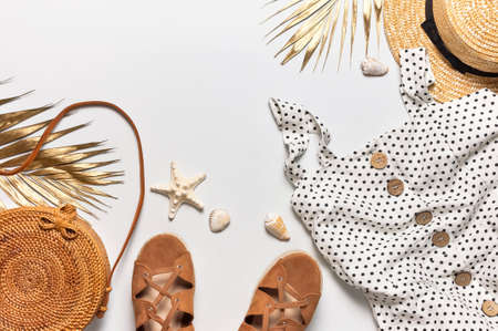 Summer womens white dress in black peas rattan woven bag brown sandals straw hat golden palm leaf shells starfish on light background. Flat lay top view. Womens beach fashion, travel vacation.の写真素材