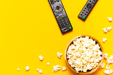 Black TV, audio remote control and popcorn on bright yellow background flat lay top view copy space....