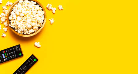 Black TV, audio remote control and popcorn on bright yellow background flat lay top view copy space. Minimalistic background with a remote control, watching a movie, series set-top boxes audio system.の写真素材