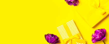 Bright yellow gift present box with ribbon and purple tulips on yellow background top view. Flat lay holiday background. Birthday present, March 8, Mother's Day, Valentine's Day. Congratulation.の写真素材