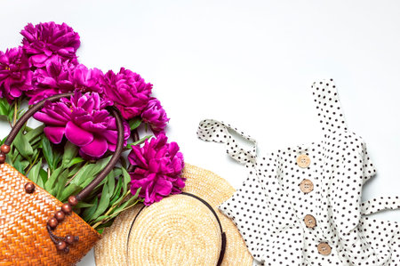Wicker straw or rattan women's eco bag with beautiful pink peonies flowers linen dress straw hat on white background. Female fashion accessory with peonies, spring summer concept, card with flowers.の写真素材