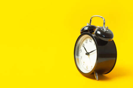 Black vintage alarm clock with white dial on yellow background flat lay copy space. Retro clock, mechanical alarm clock. Minimalistic background, concept of time, deadline, time to work, morning.の写真素材