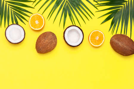Summer tropical composition. Green tropical leaves of palm trees, coconut, orange on bright yellow background. Flat lay, top view, copy space. Creative background food, fruit.の写真素材