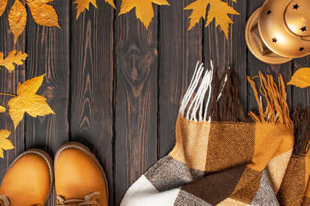 Autumn Fashion Concept. Brown Orange leather women boots with fur, checkered warm plaid, golden autumn leaf, decorative golden lamp on brown wooden background top view. Fashionable womens footwear.の写真素材