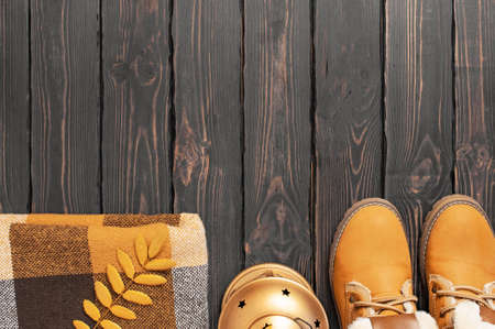 Autumn Fashion Concept. Brown Orange leather women boots with fur, checkered warm plaid, golden autumn leaf on brown wooden background top view. Fashionable womens footwear. Cozy fall composition.の写真素材