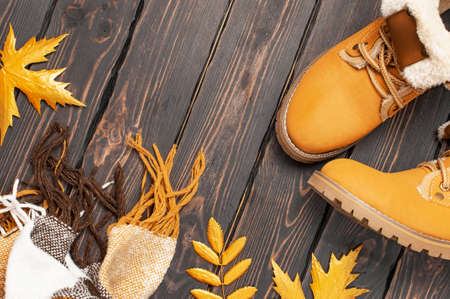 Autumn Fashion Concept. Brown Orange leather women boots with fur, checkered warm plaid, golden autumn leaf on brown wooden background top view. Fashionable womens footwear. Cozy fall composition.の写真素材
