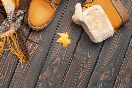 Autumn Fashion Concept. Brown Orange leather women boots with fur, checkered warm plaid, golden autumn leaf on brown wooden background top view. Fashionable womens footwear. Cozy fall composition.の写真素材