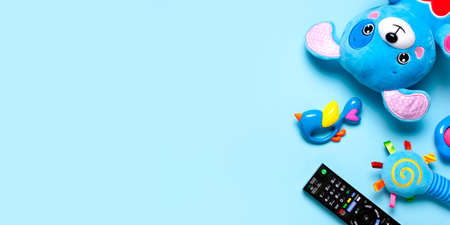 Black TV audio remote control and baby toys rattles, toy puppy on blue background flat lay top view copy space. Concept of viewing childrens television shows, cartoons, childrens films. Home leisure.の写真素材