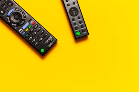 Black TV and audio remote control on bright yellow background flat lay top view copy space. Minimalistic background with a remote control, watching TV, set-top boxes, audio system, soundbar.の写真素材