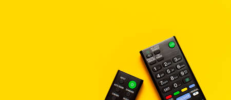 Black TV and audio remote control on bright yellow background flat lay top view copy space. Minimalistic background with a remote control, watching TV, set-top boxes, audio system, soundbar.の写真素材