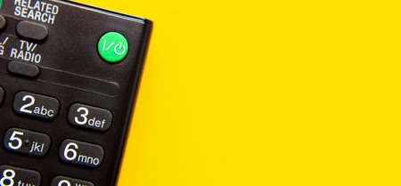 Black TV remote control on bright yellow background flat lay top view copy space. Minimalistic background with a remote control, watching TV, set-top boxes, audio system, soundbar.の写真素材