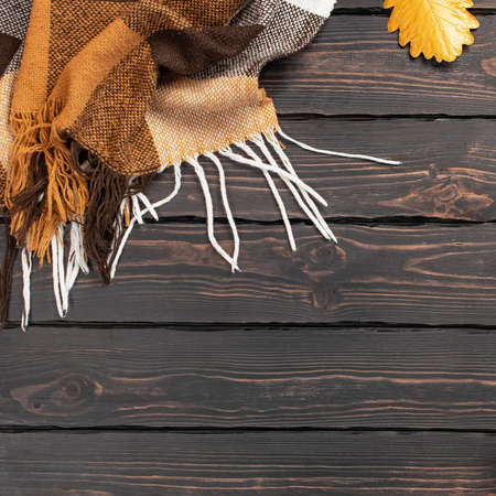 Woolen checkered plaid. Autumn background. Checkered yellow brown plaid with golden leaves on dark wooden background top view. Cozy fall composition.の写真素材