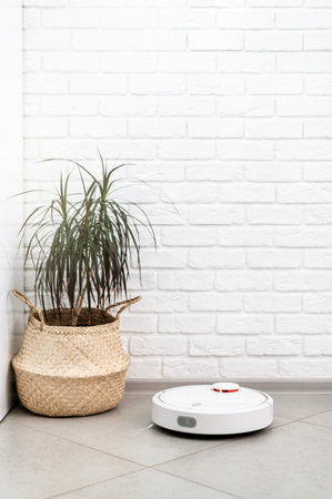 Home Cleaning Concept. Modern robot vacuum cleaner cleans houses on porcelain tiles against a brick...