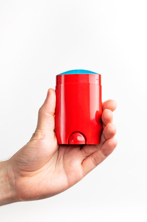 Red deodorant in male hand isolated on white background. Men's deodorant, personal hygiene products, men's cosmetics. Red clean plastic deodorant packaging, mockup for advertising, place for text.の写真素材