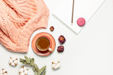 Flat lay autumn composition. Cup of coffee pink knitted women's sweater or warm plaid cotton flowers dry rose eucalyptus macaroon cake blank notebook pencil on white background top view. fall concept.の写真素材