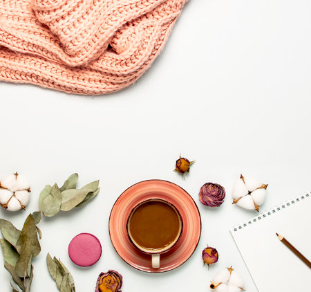 Flat lay autumn composition. Cup of coffee pink knitted women's sweater or warm plaid cotton flowers dry rose eucalyptus macaroon cake blank notebook pencil on white background top view. fall concept.の写真素材