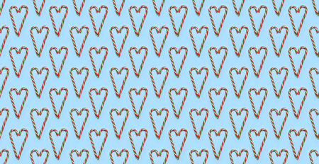Seamless Pattern of Traditional Christmas candy cane lollipop shape of heart on blue background flat...