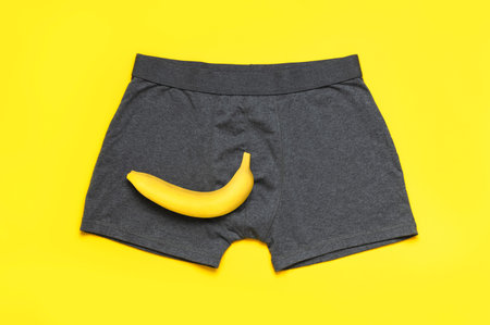 Creative concept of male potency. Gray cotton panties, fresh banana on yellow background flat lay...