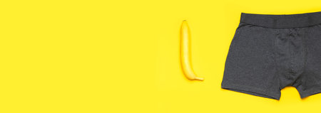 Creative concept of male potency. Gray cotton panties, fresh banana on yellow background flat lay...