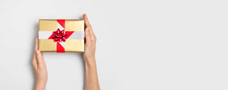 New Year and Christmas 2021 banned. Golden gift with prohibiting red and white tape in female hands on gray background flat lay top view. Holidays in quarantine. Coronavirus 2019-nCoV. Stay at home.の写真素材