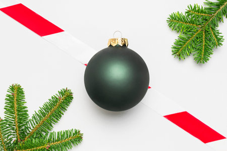 Concept for new year and christmas 2021 during the Coronavirus 2019-nCoV. Green ball, fir branches, prohibition tape on light background flat lay top view. Stay at home. Quarantine. Banning holiday.の写真素材