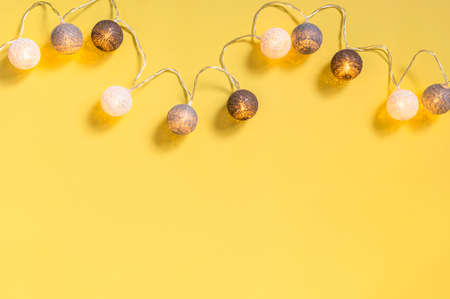 Gray white festive garland on yellow background flat lay top view. Cotton Balls Garland. Round bulbs LED festoon lights electric garland. Festive decoration Colors year 2021 Illuminating Ultimate grey.の写真素材