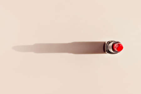 Red lipstick on beige background flat lay top view copy space. Beauty and cosmetics background. Decorative cosmetics, makeup, women's lipstick, beauty brand, product design.の写真素材
