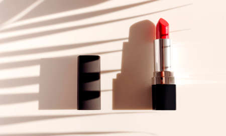 Red lipstick sun shadows from palm leaf on beige background flat lay top view copy space. Beauty and cosmetics background. Decorative cosmetics, makeup, women's lipstick, beauty brand product design.の写真素材