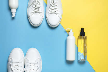 White leather sneakers, plastic bottles of cleaning products for shoes on blue yellow background flat lay top view. Natural leather shoe care, spray, foam, shoe deodorant, cosmetic shoe products.の写真素材