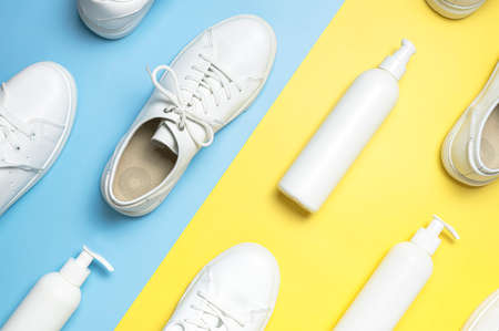 White leather sneakers, plastic bottles of cleaning products for shoes on blue yellow background flat lay top view. Natural leather shoe care, spray, foam, shoe deodorant, cosmetic shoe products.の写真素材